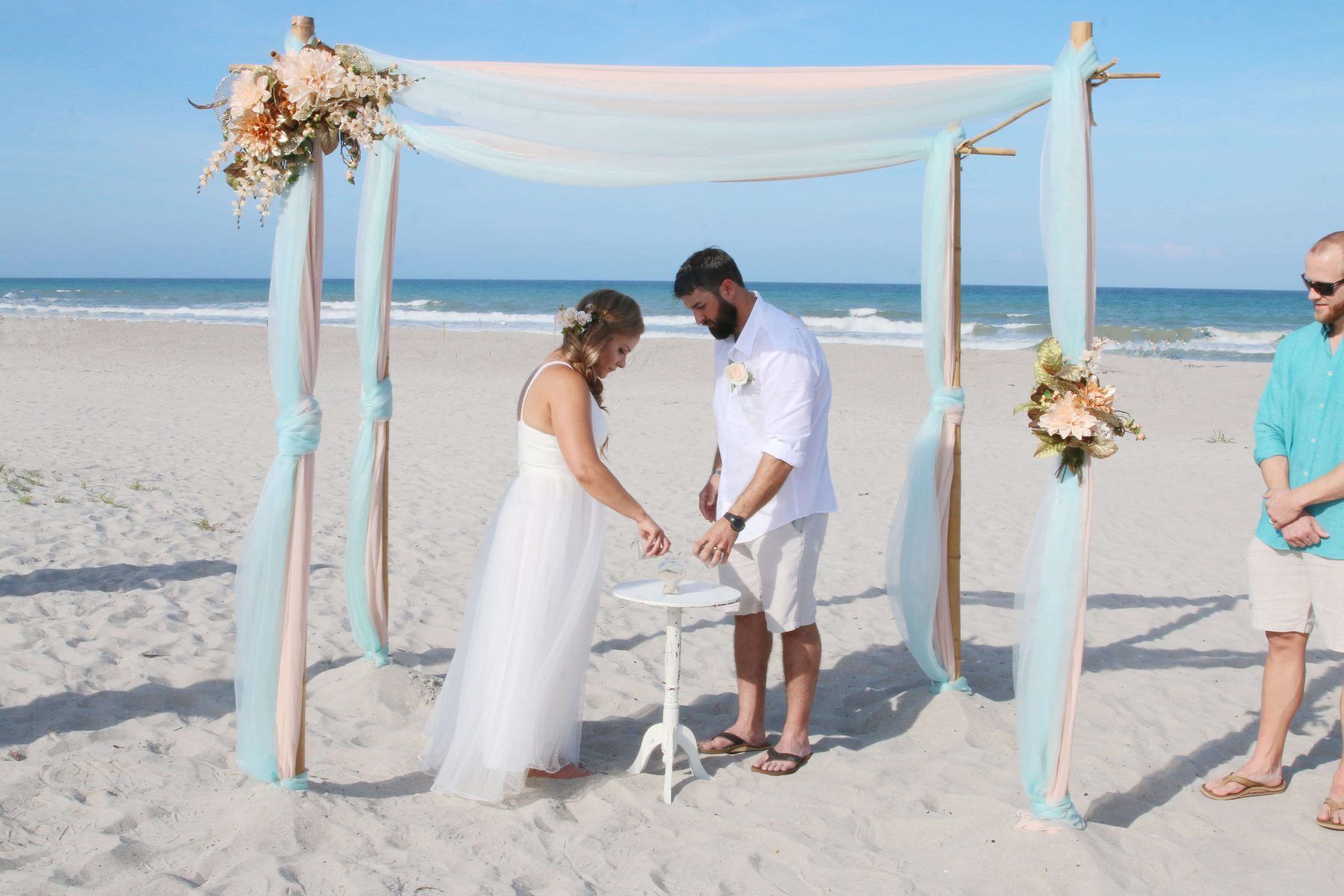 Couple pouring sand during a beach wedding ceremony, with ocean in the background.