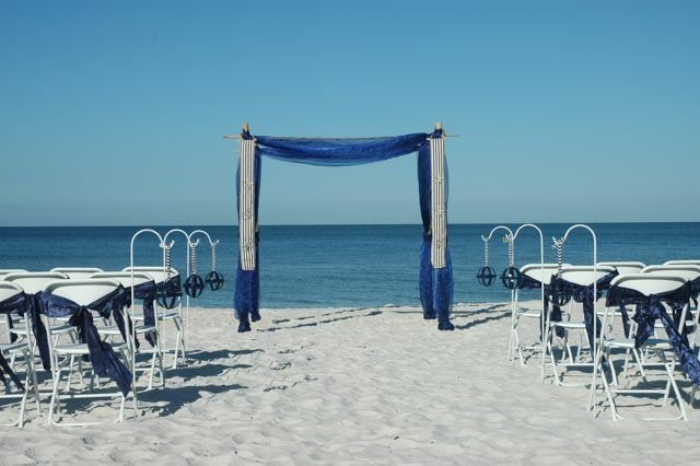 Beach wedding setup with white chairs, blue draping, and ocean backdrop.