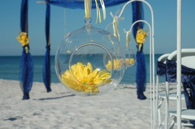 Clear glass globe with yellow flower hanging at a beach wedding ceremony, blue and white decor.