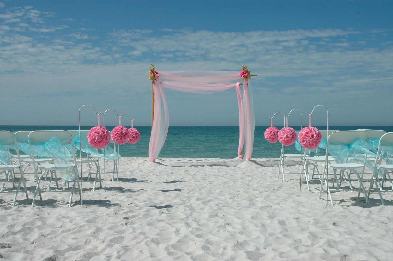 Beach wedding ceremony setup with pink and turquoise decor.