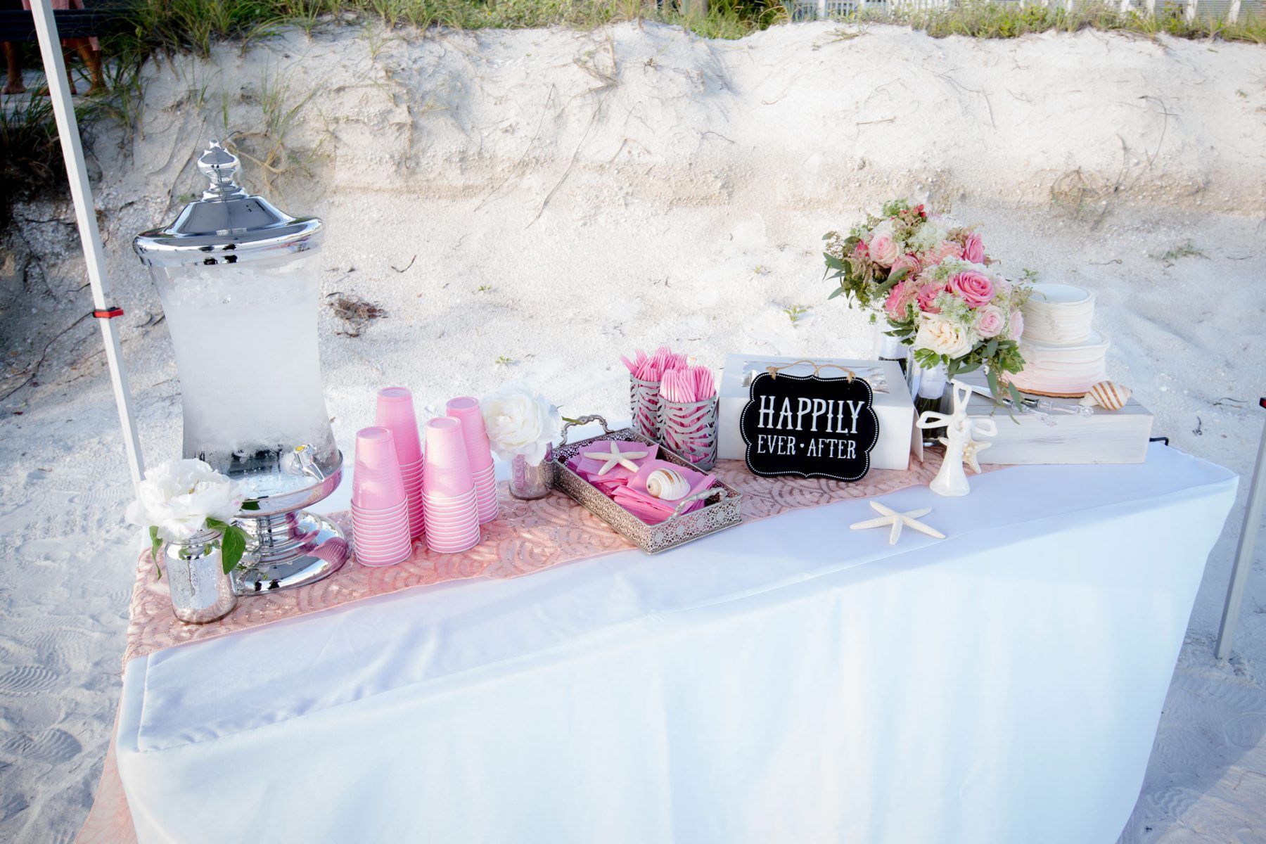 Wedding reception drink station on a beach with pink accents.