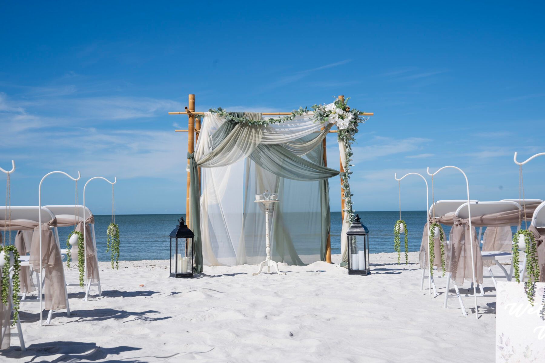 Beach wedding setup with a draped altar, seating, and ocean backdrop.