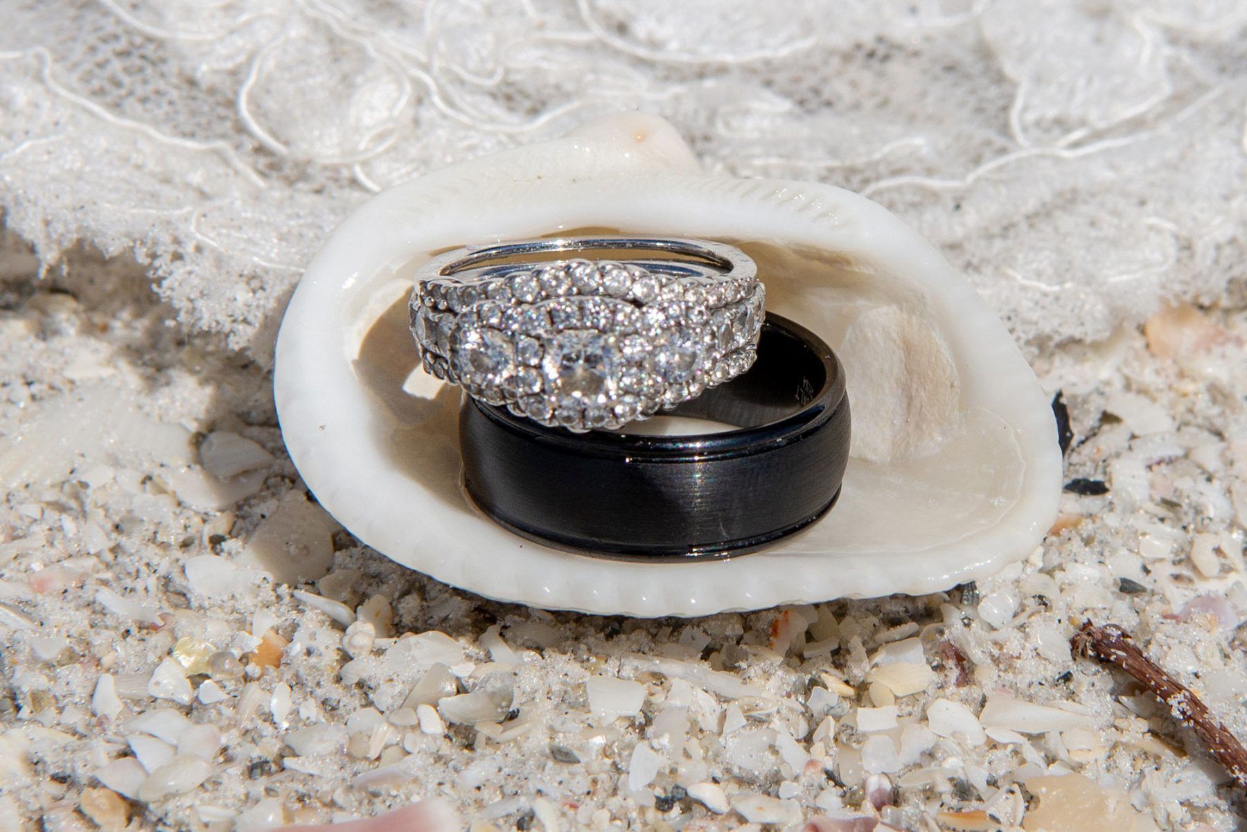 Wedding rings in a seashell on sand, with lace background.
