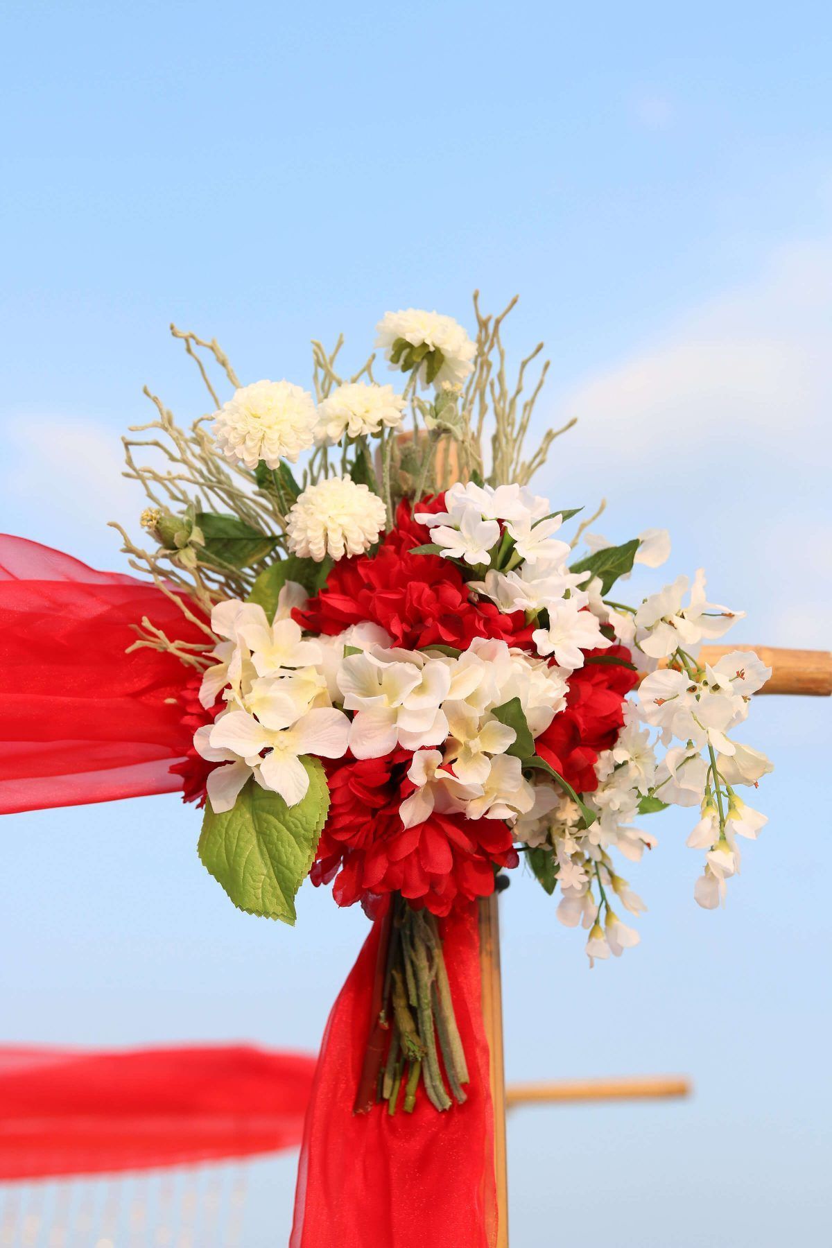 Floral arrangement on red fabric, against a blue sky, includes red, white, and green flowers.