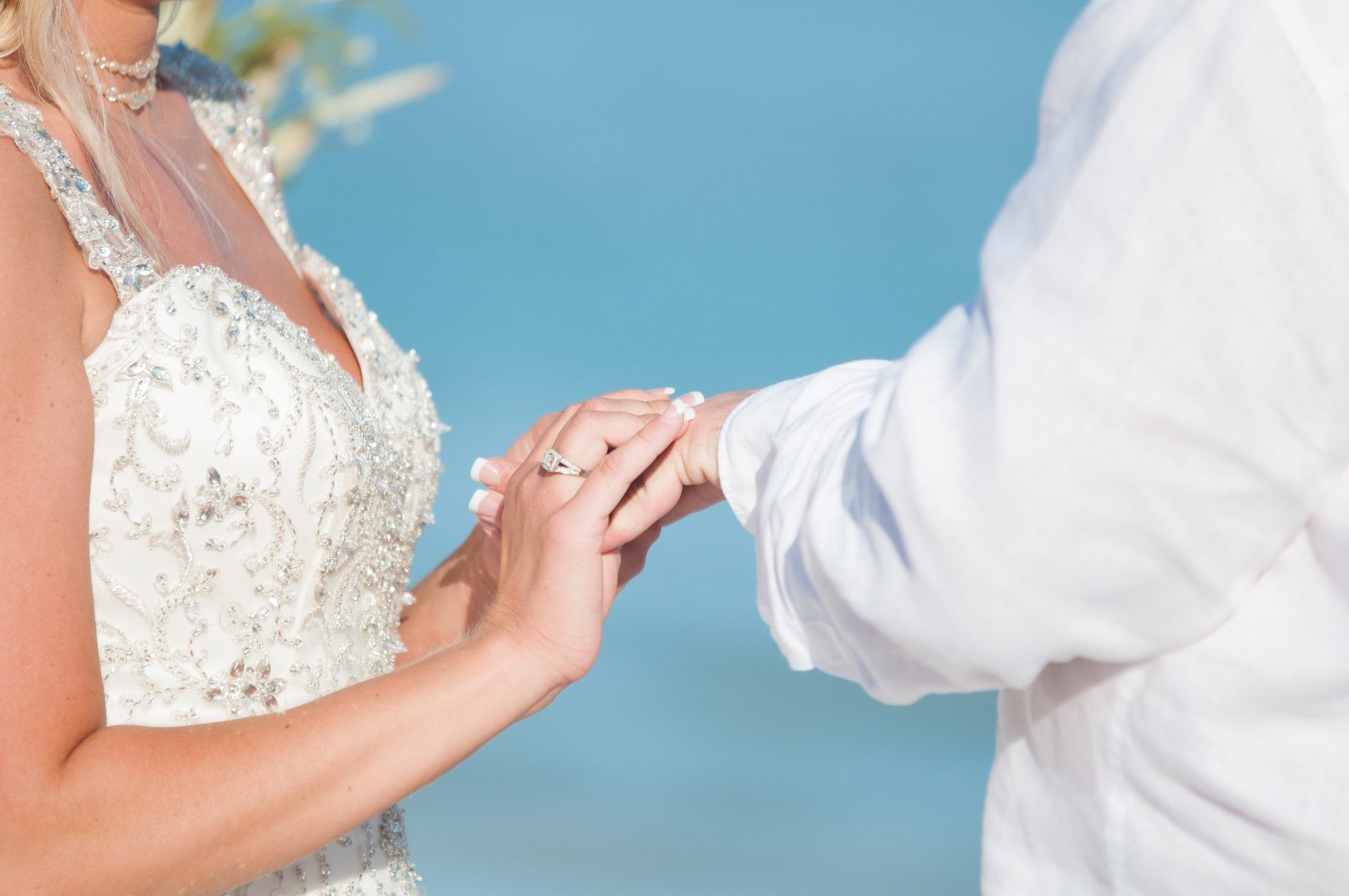 Bride and groom holding hands during a beach wedding; blue ocean in background.
