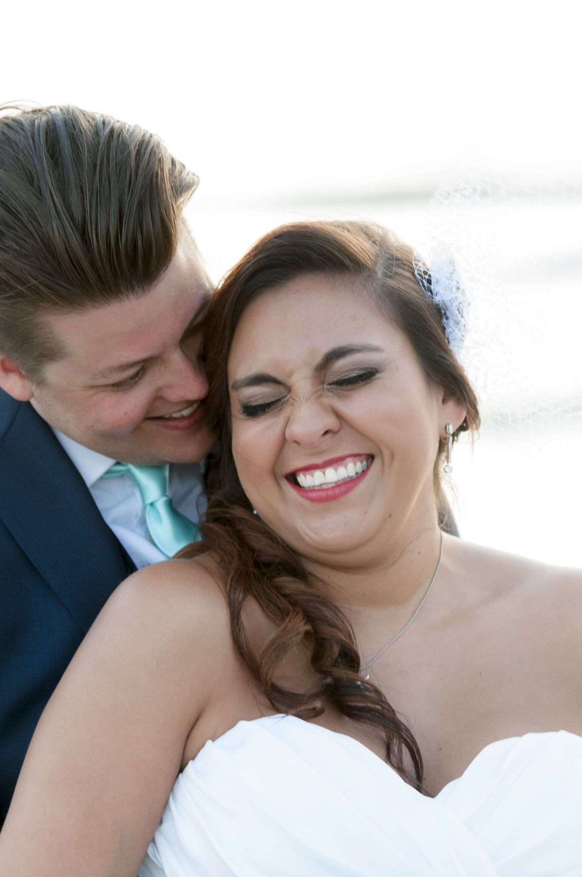 Couple laughing, bride in strapless white dress, groom in blue suit with turquoise tie.