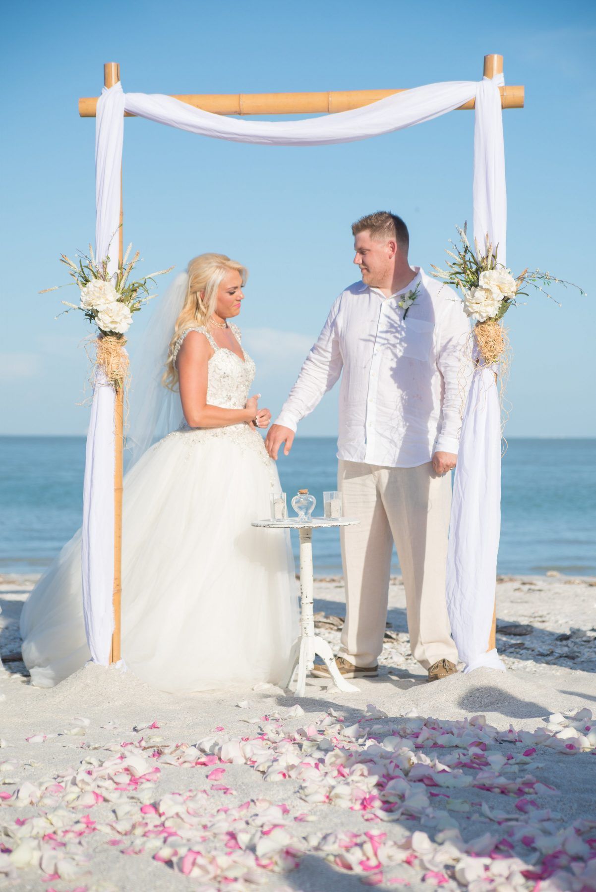 Couple holding hands during beach wedding ceremony under bamboo arch.