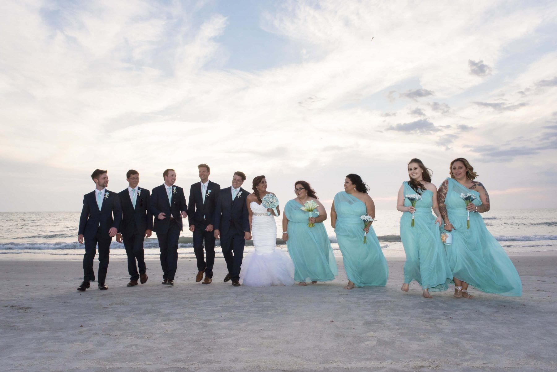 Wedding party on a beach. Bride and groom with bridesmaids and groomsmen in formal attire, walking near the water.