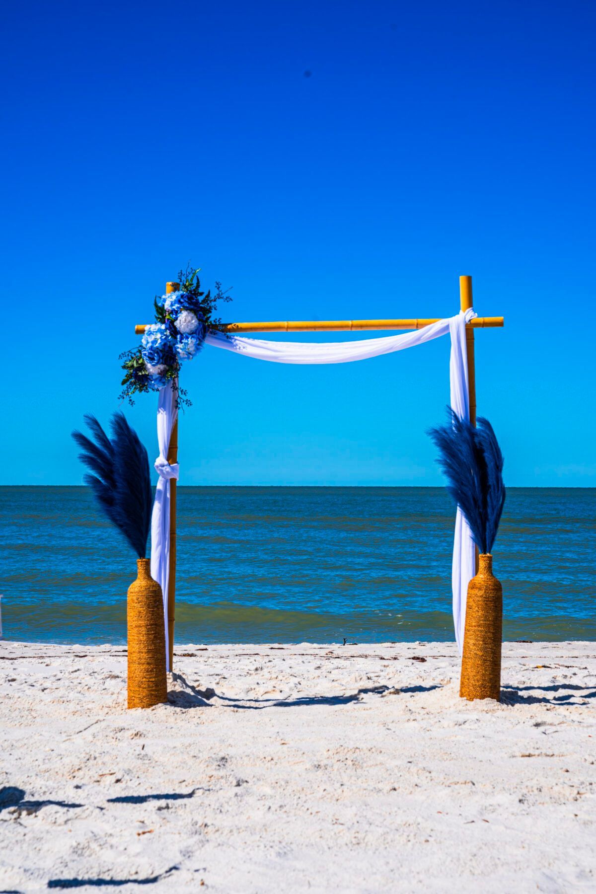 Wedding arch on a beach with blue decorations and ocean backdrop.