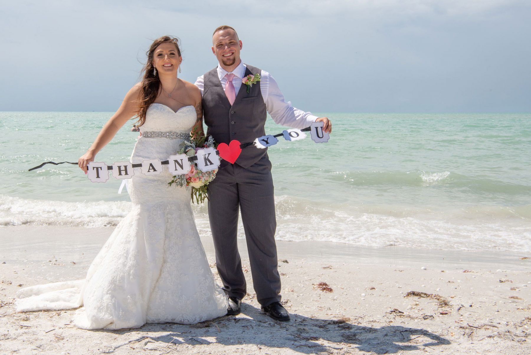 Newlyweds on a beach holding a banner that says 