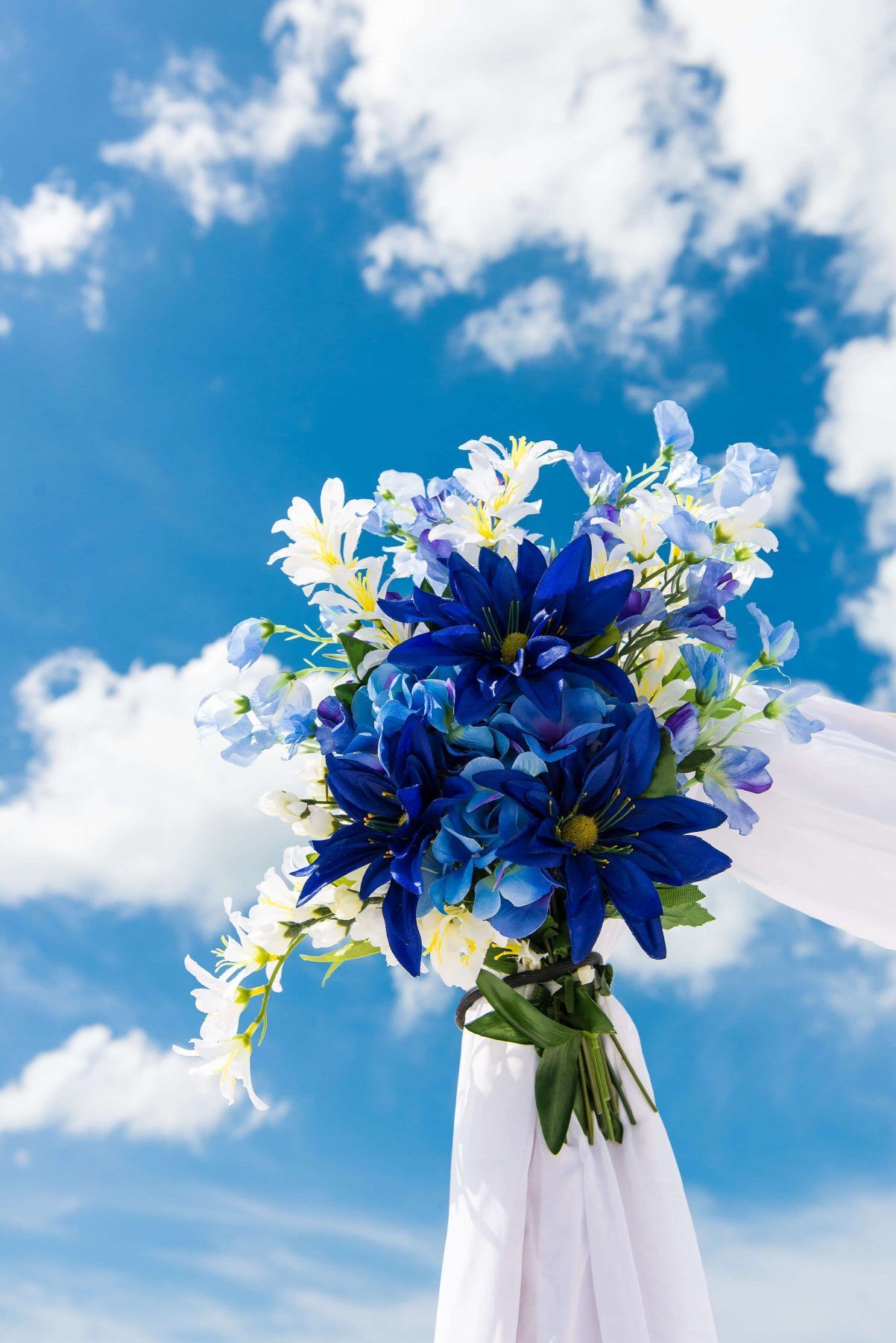 Blue and white flower bouquet against a bright blue sky with white clouds, part of a draped structure.