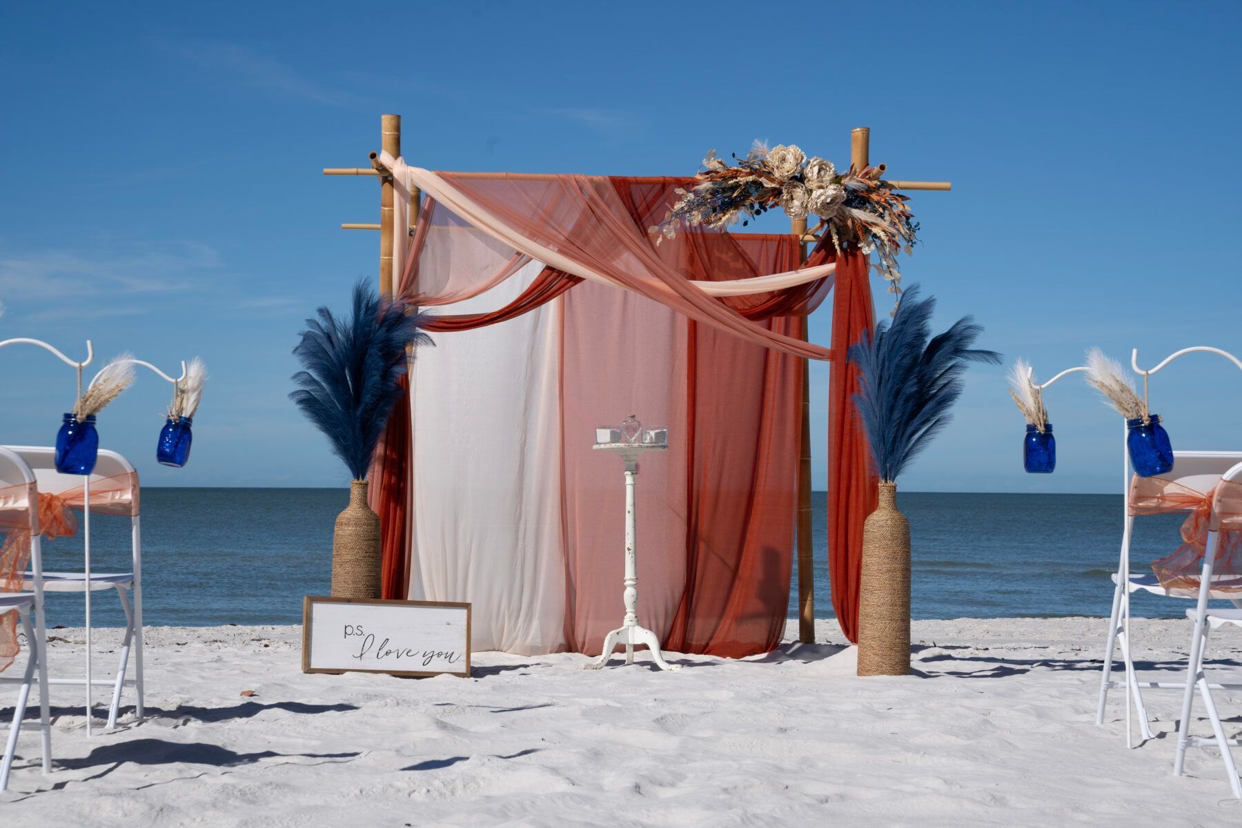 Beach wedding ceremony setup with coral and navy decorations.