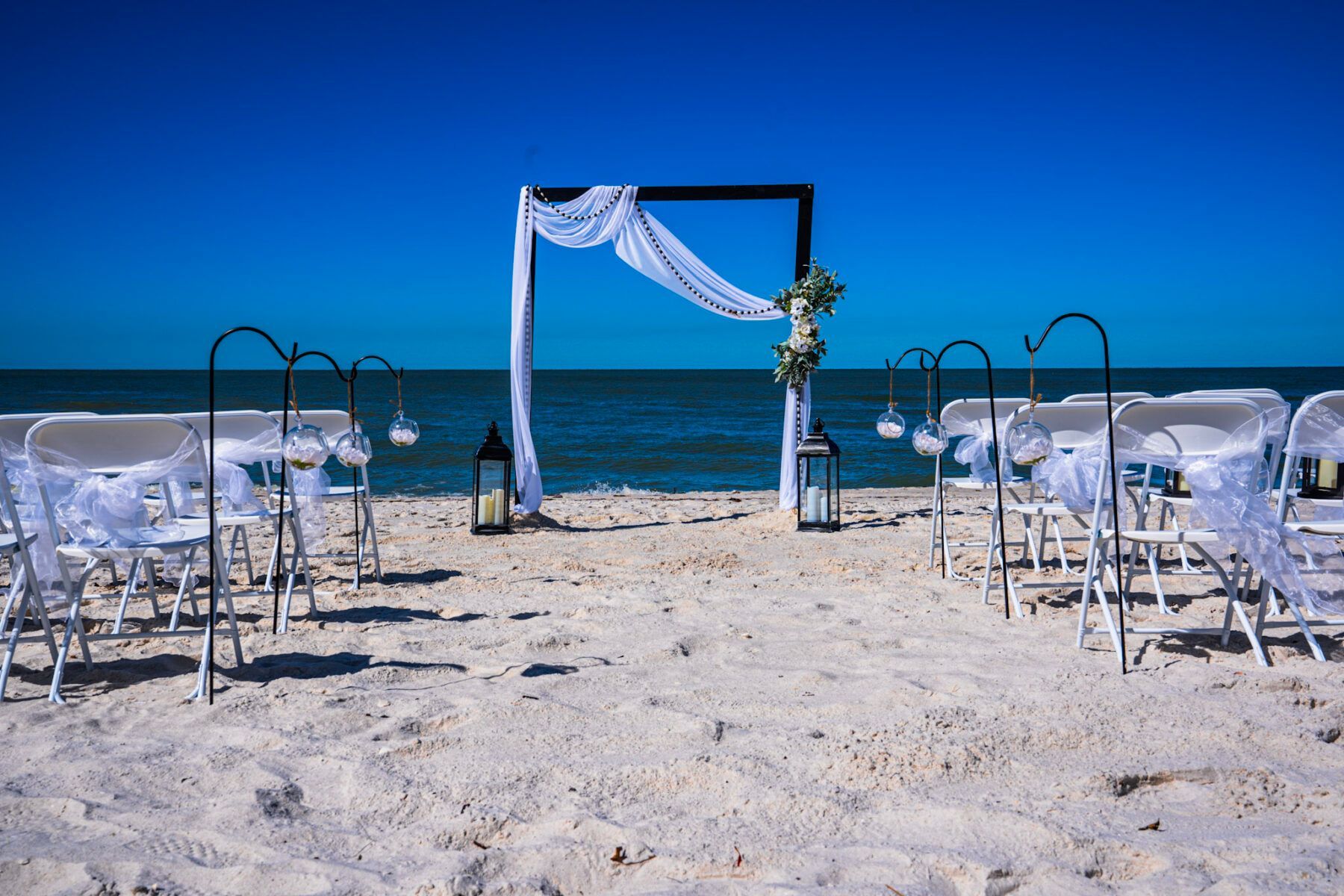 Beach wedding ceremony setup with white chairs, arch, and ocean view.