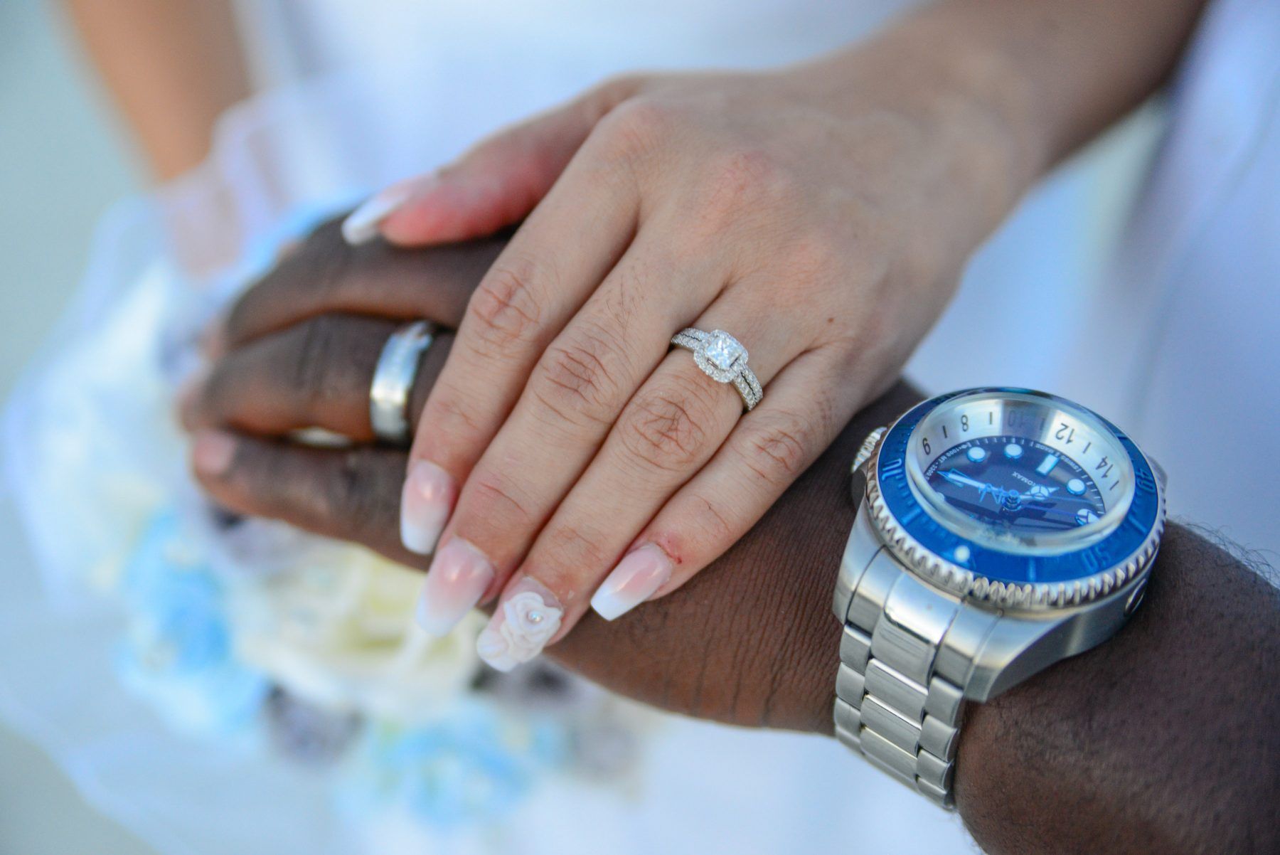 Close-up of hands with rings: a silver wedding band, a diamond engagement ring, and a wristwatch with a blue bezel.