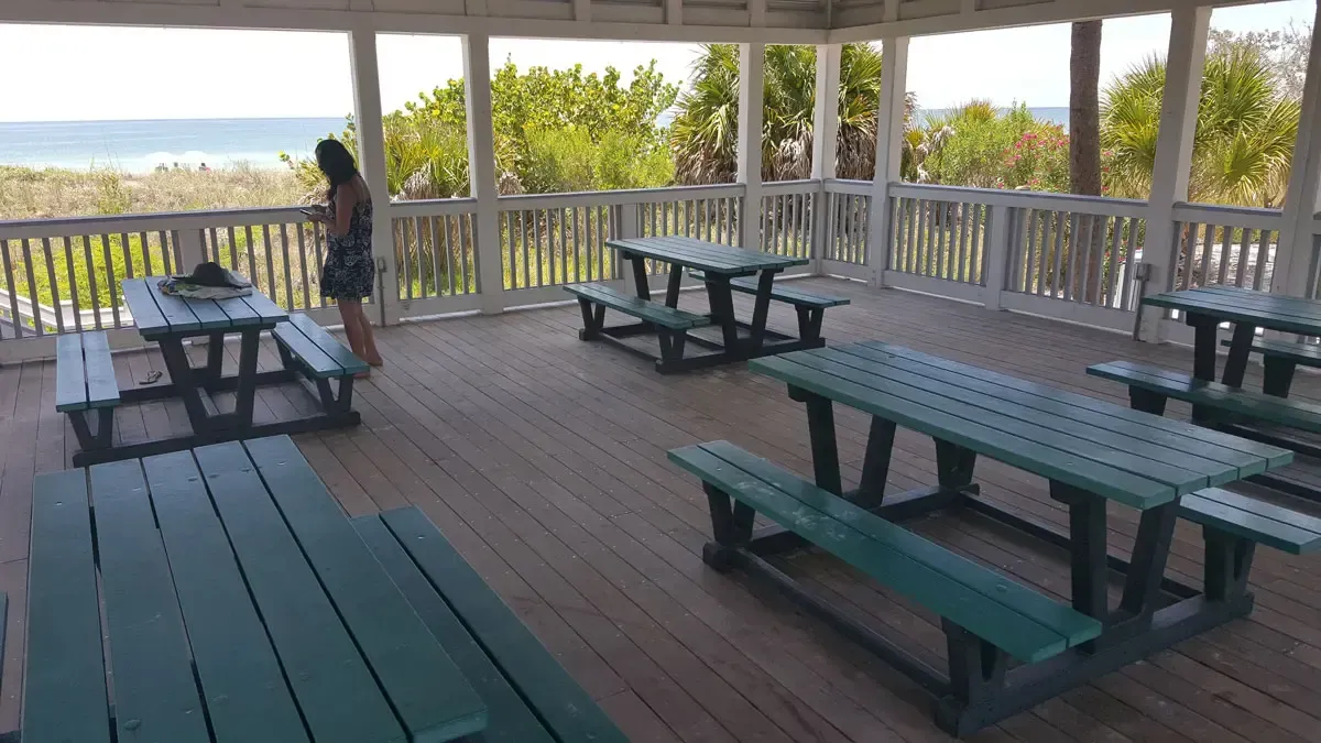 Wooden gazebo with picnic tables overlooking the ocean; a person stands near a table.