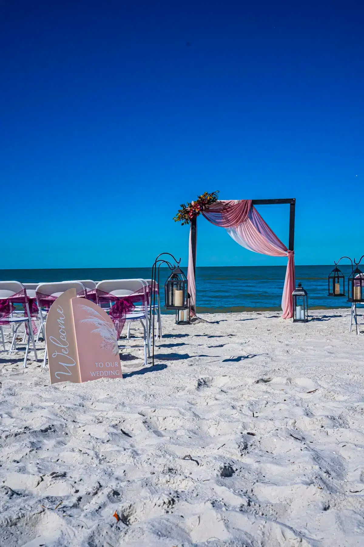 Beach wedding setup with chairs, arch, and ocean view on a sunny day.