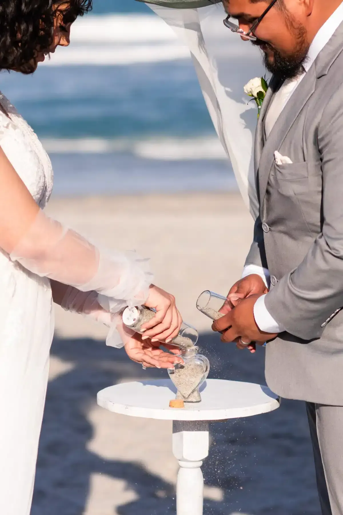 Couple pouring sand into a unity vase on a beach during a wedding ceremony.