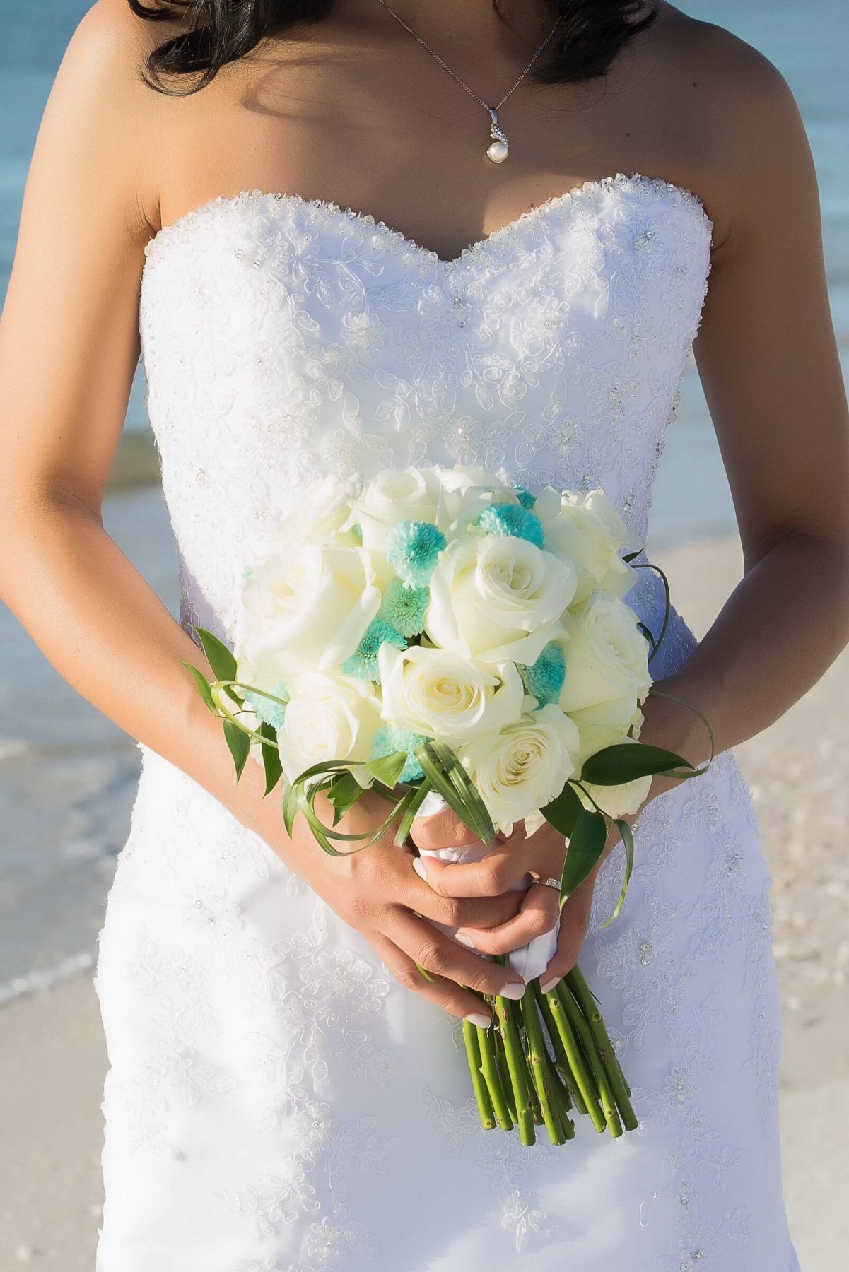 Bride holding white and teal flower bouquet; on beach.