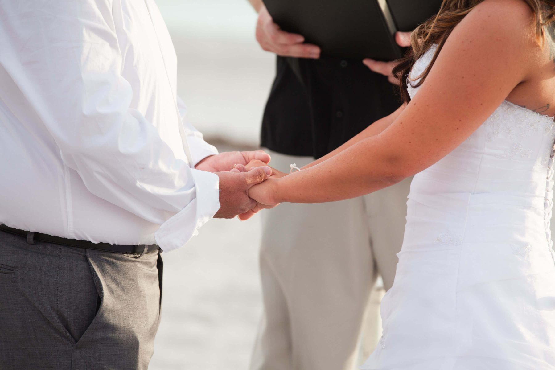 Couple holding hands during beach wedding ceremony.