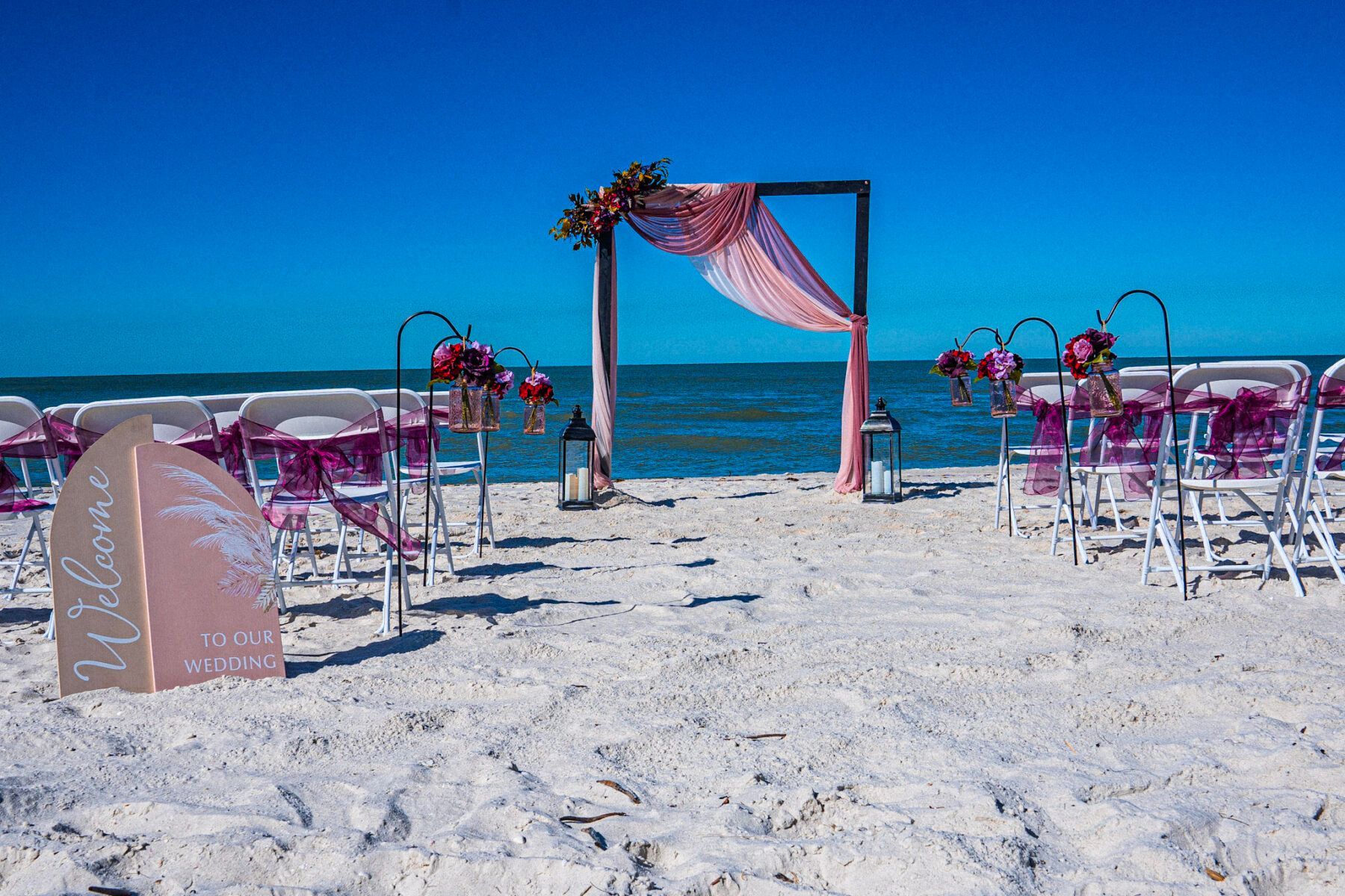 Beach wedding ceremony setup with pink accents and a clear blue sky.