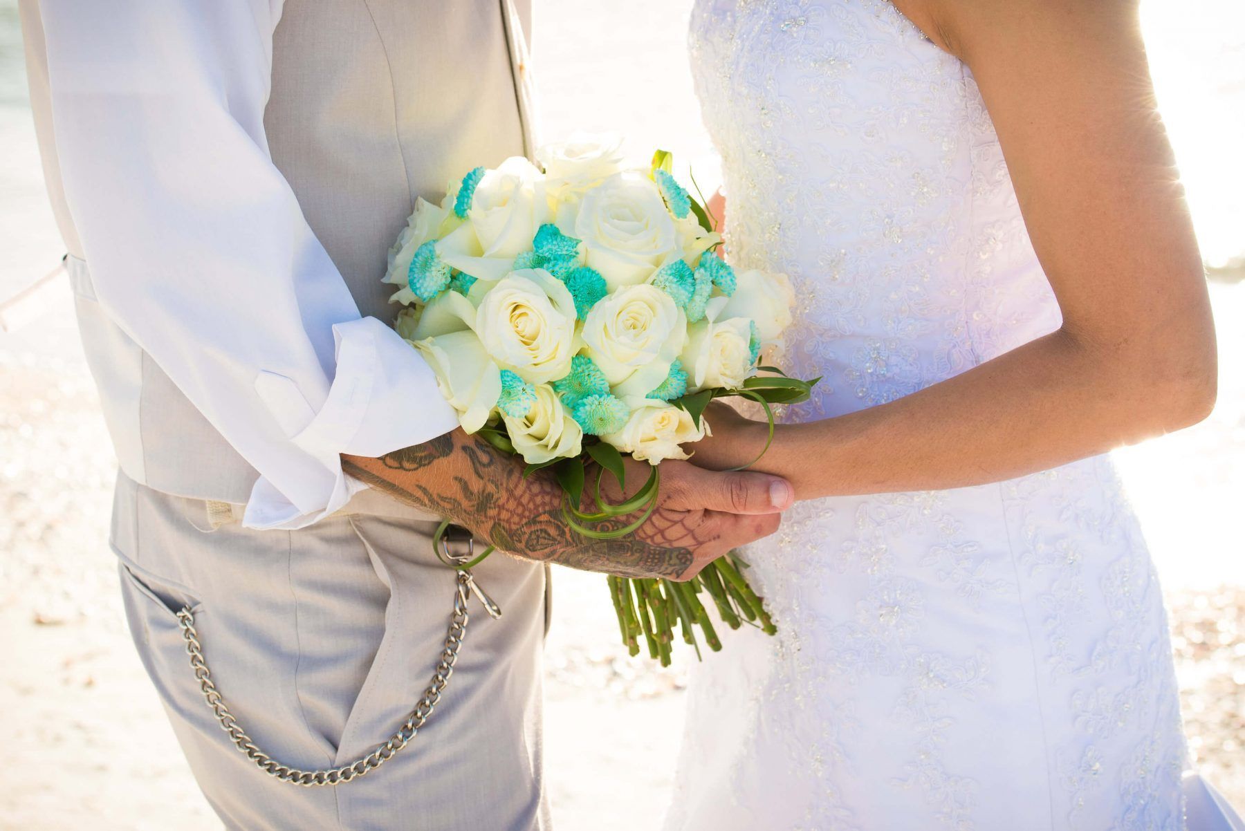 Bride and groom holding hands, bride in white dress, groom in vest with bouquet of white and blue flowers.