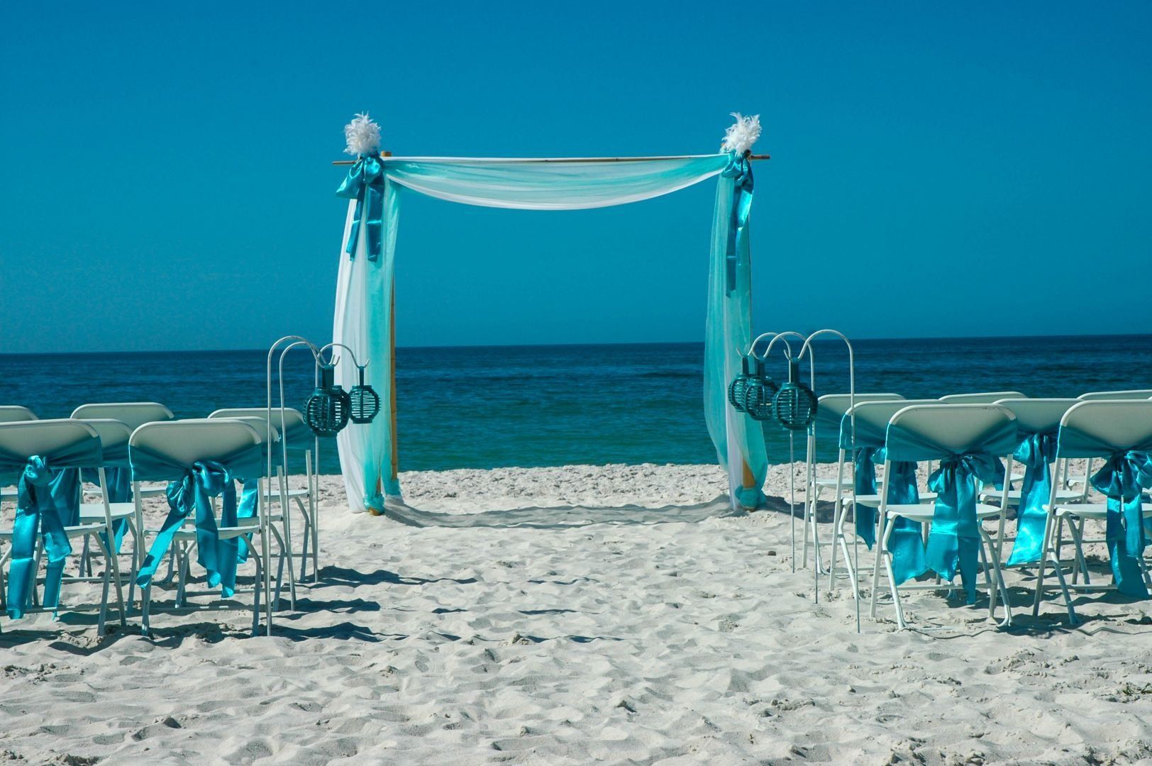 Beach wedding setup with turquoise decorations and ocean backdrop.