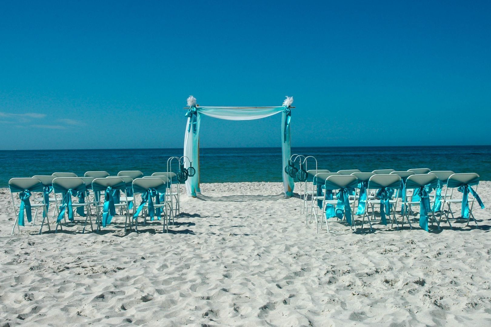Beach wedding setup with turquoise decorations and ocean backdrop.