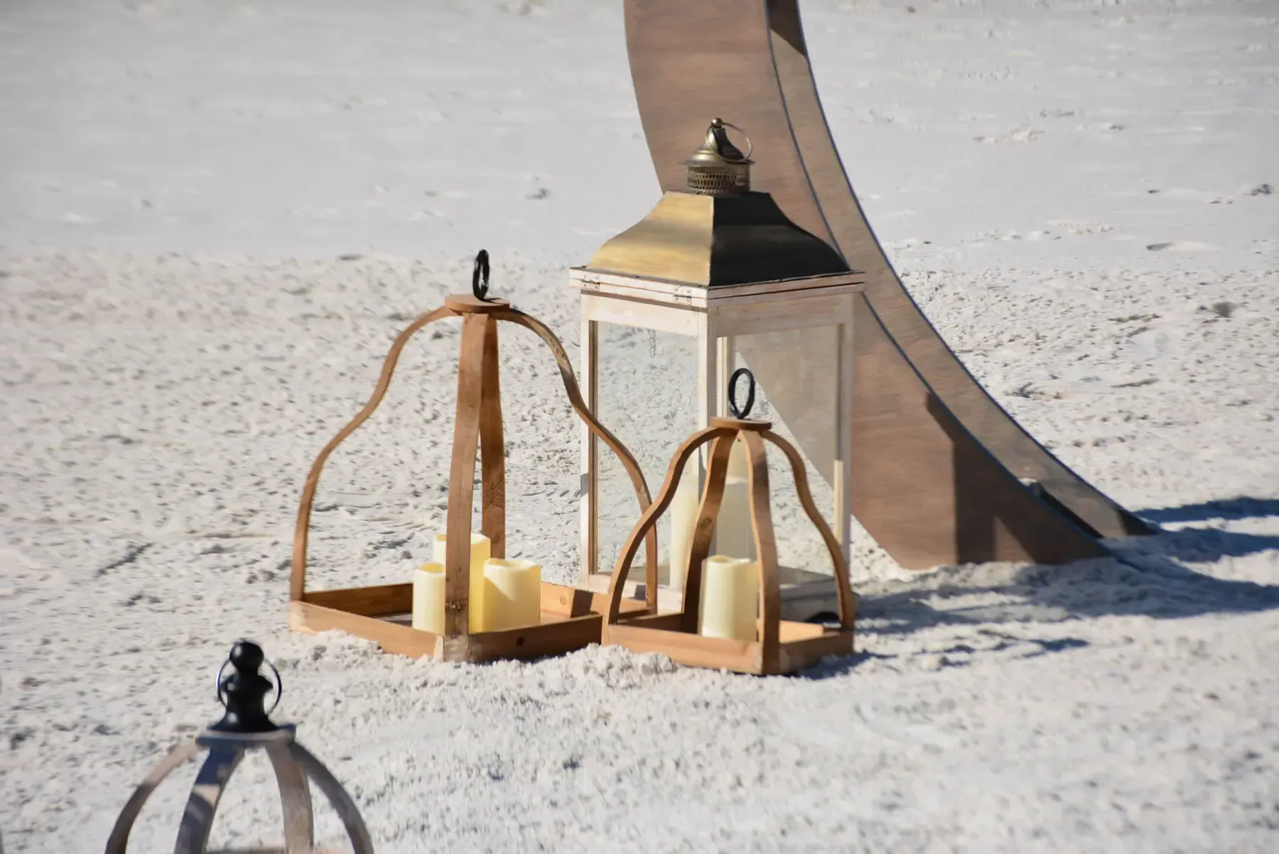 Wooden lanterns with candles on white sand near a wooden arch.