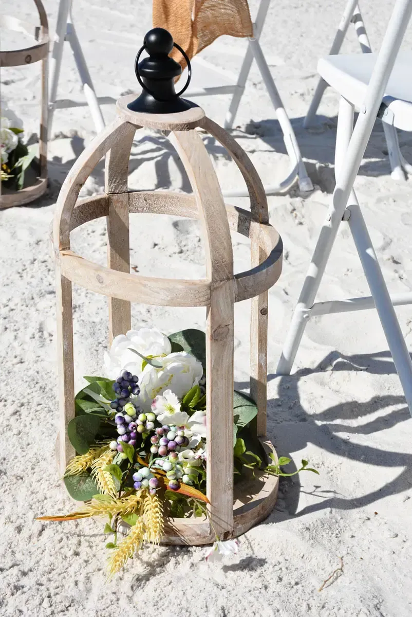 Wooden lantern with flowers on sand, set up for a beach wedding.