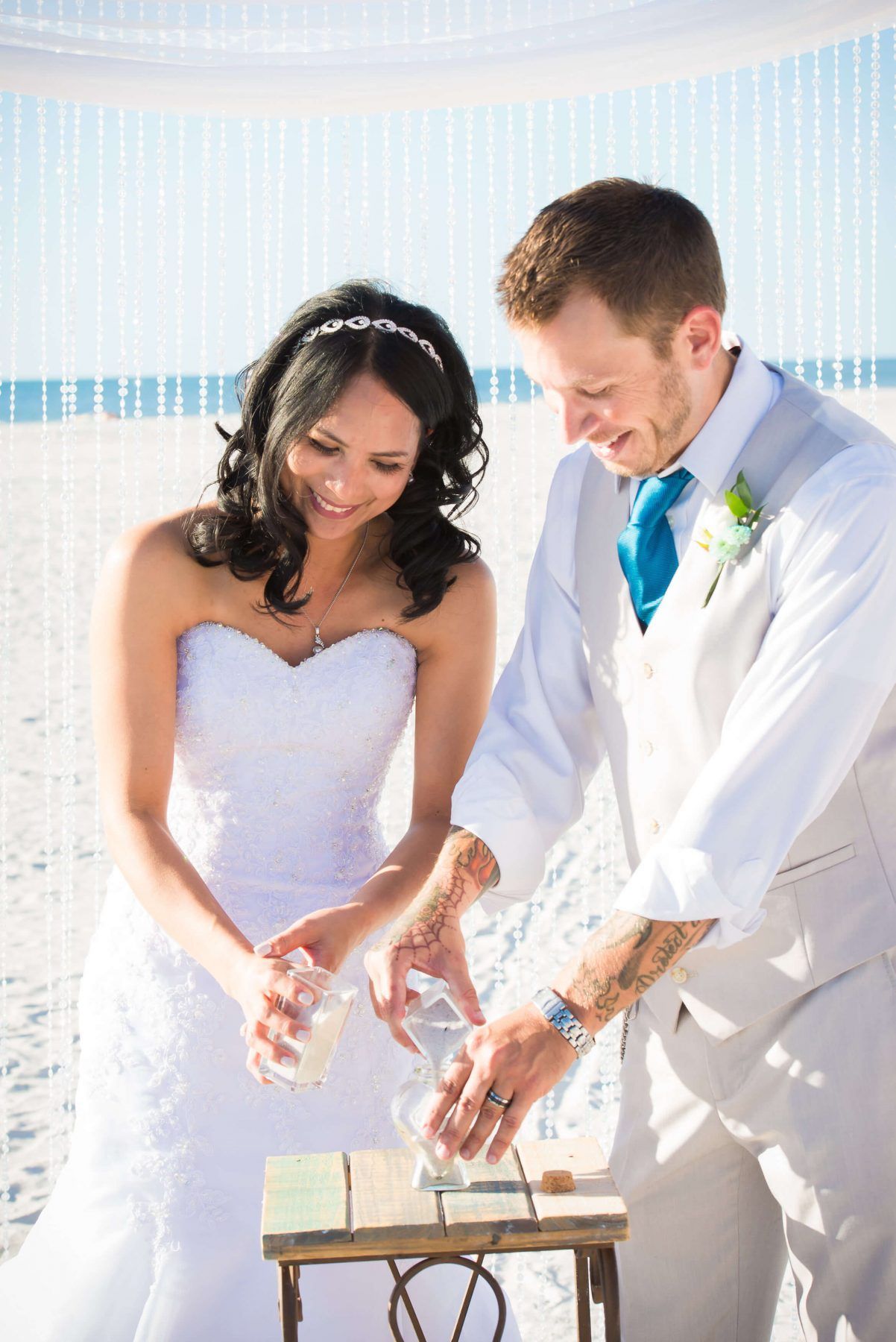 Couple pouring sand into a unity vase during a beach wedding ceremony.