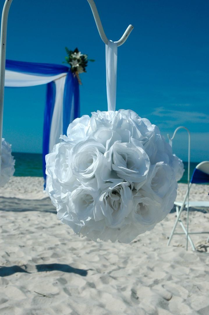 White floral ball hanging on a metal stand, beach wedding scene, blue sky and ocean.