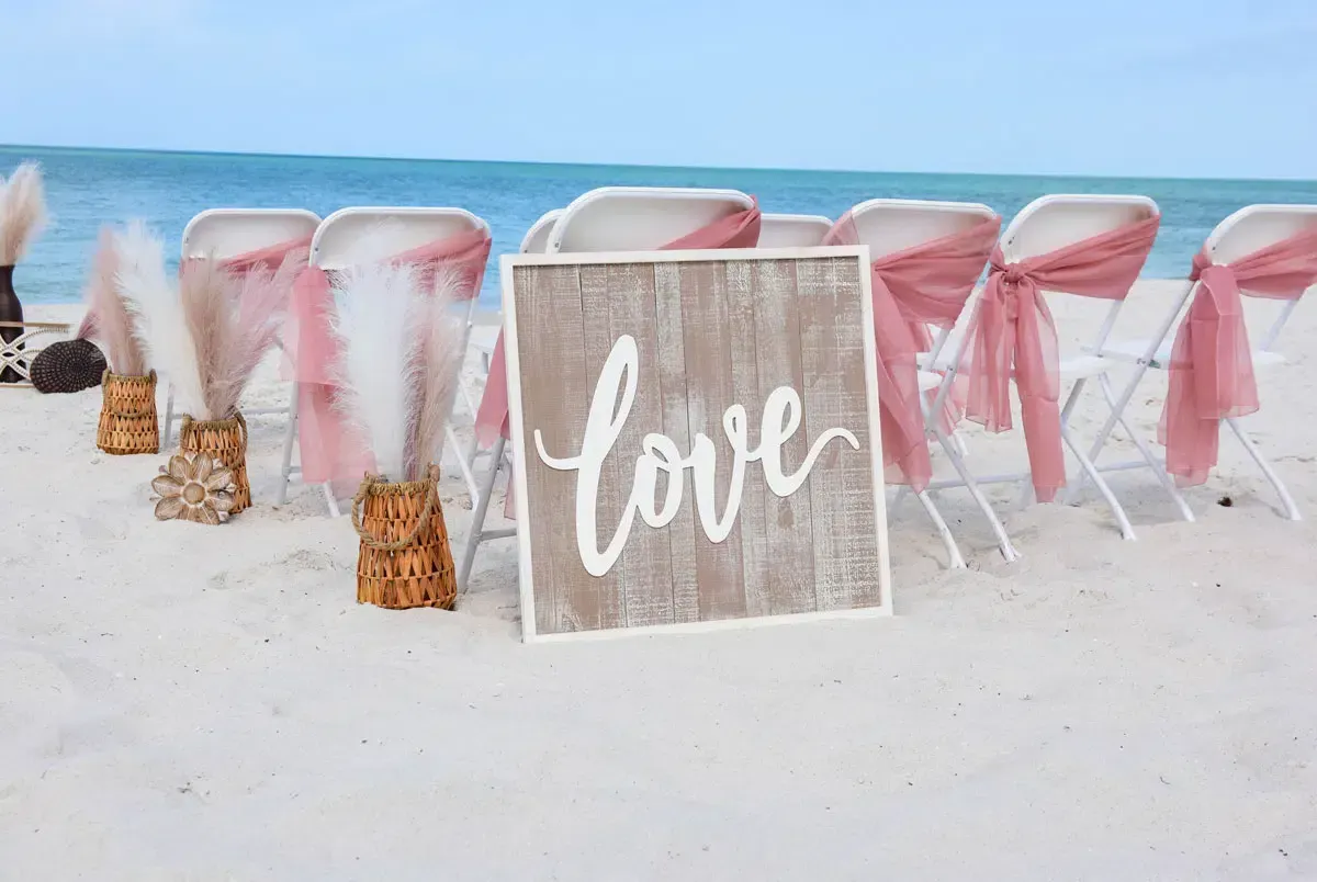 Beach wedding setup with chairs, pink sashes, 