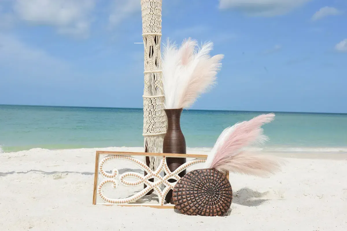 Beach wedding decor with pampas grass, wood, and a clear blue sky.