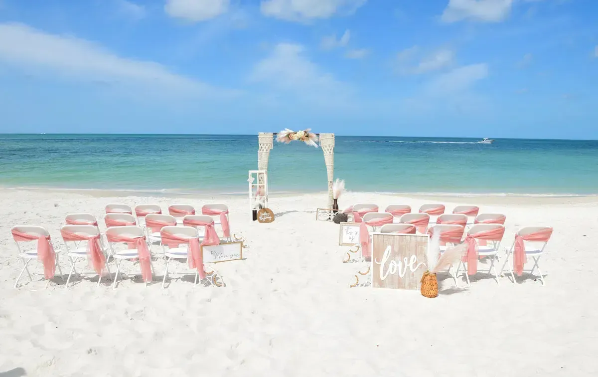 Beach wedding ceremony with chairs, arch, and 