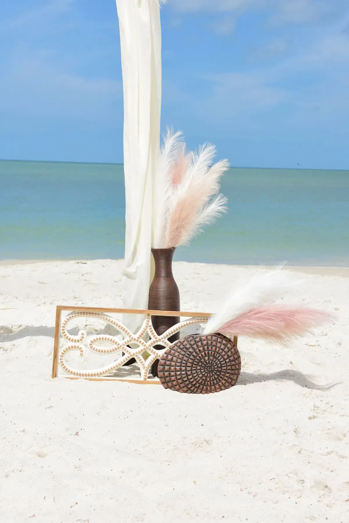 Beach wedding decor with pampas grass, white sand, and ocean backdrop.