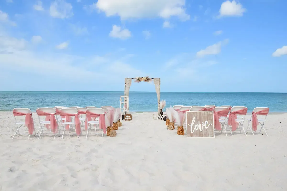 Beach wedding setup with chairs, a decorated arch, and a 