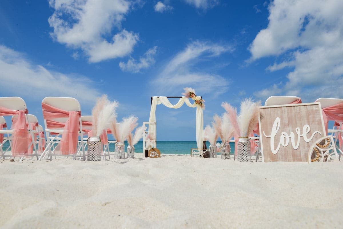 Beach wedding setup with chairs, an arch, and