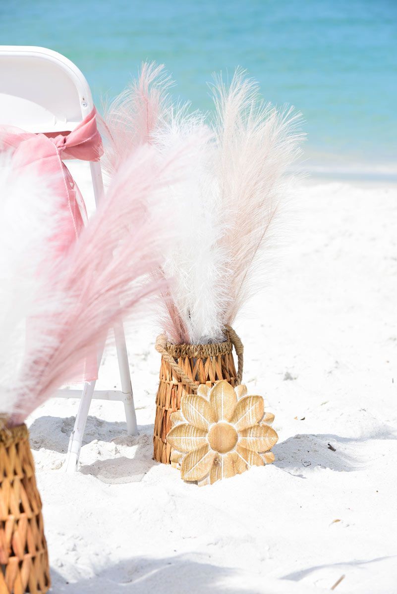 Beach wedding decor with white chair, pink fabric, and pampas grass in a woven basket.
