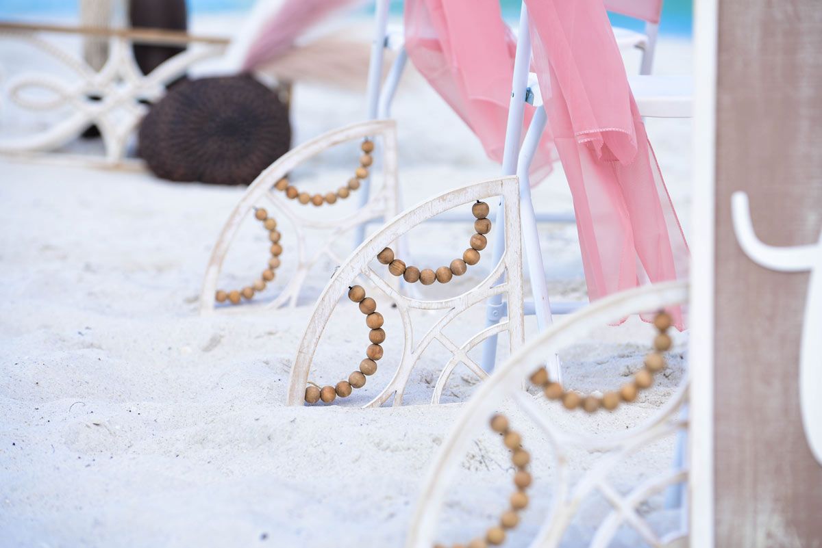 Beach wedding chairs with clear backs, decorated with beads and pink fabric.