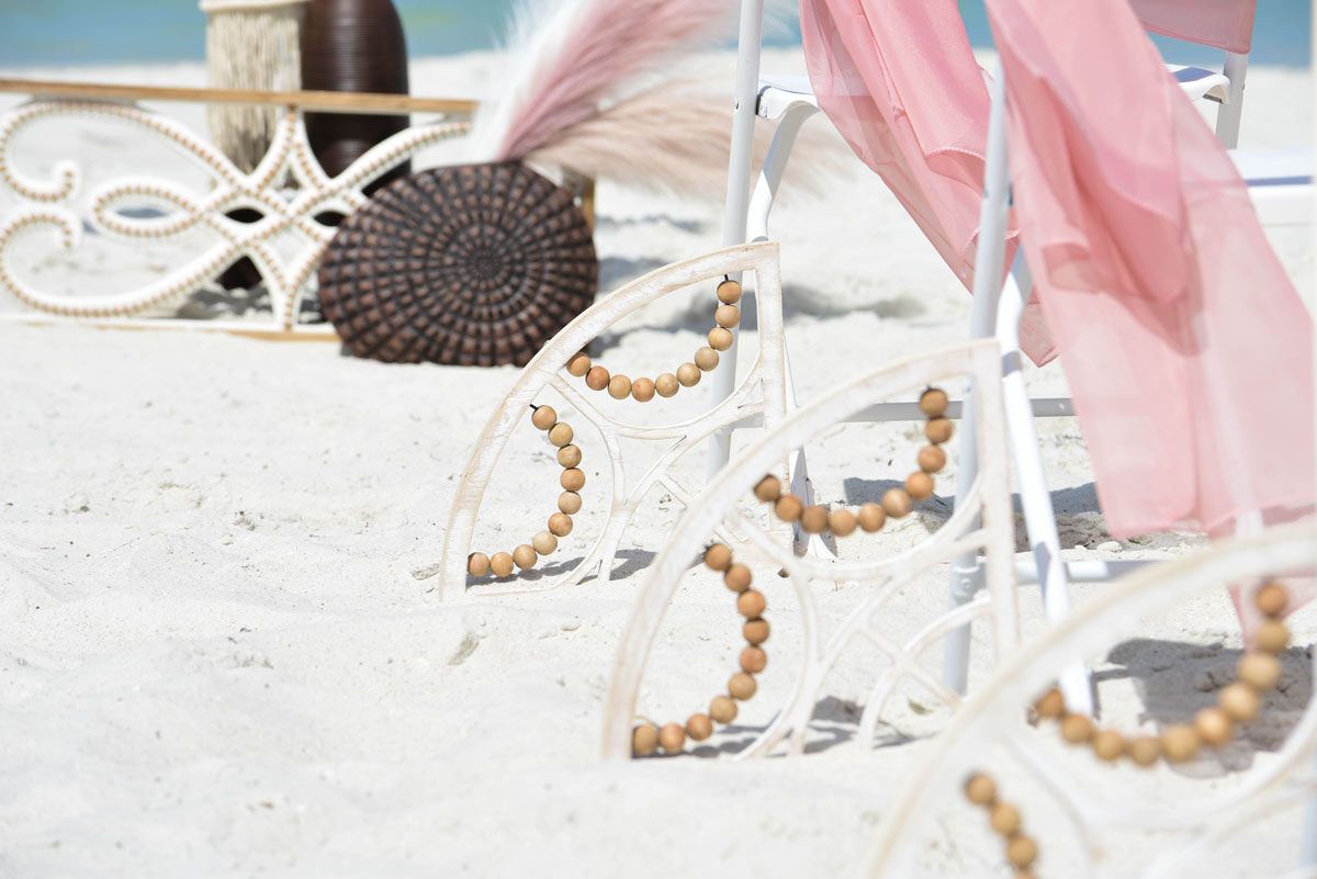 Beach wedding setup with chairs, pink draping, and decorative items on white sand.