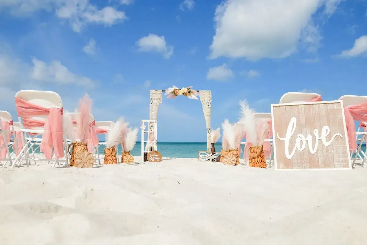 Beach wedding setup with white chairs, pink accents, and 
