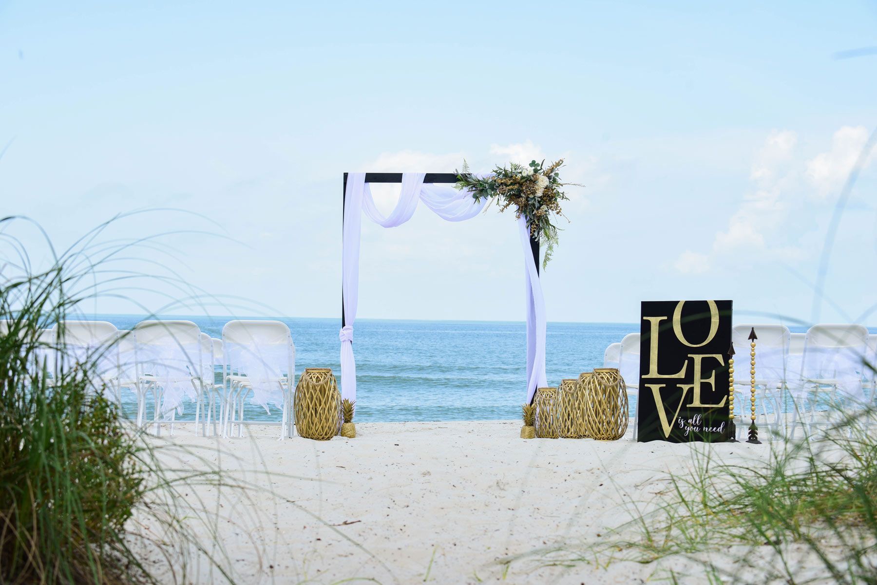 Beach wedding setup with arch draped in white,