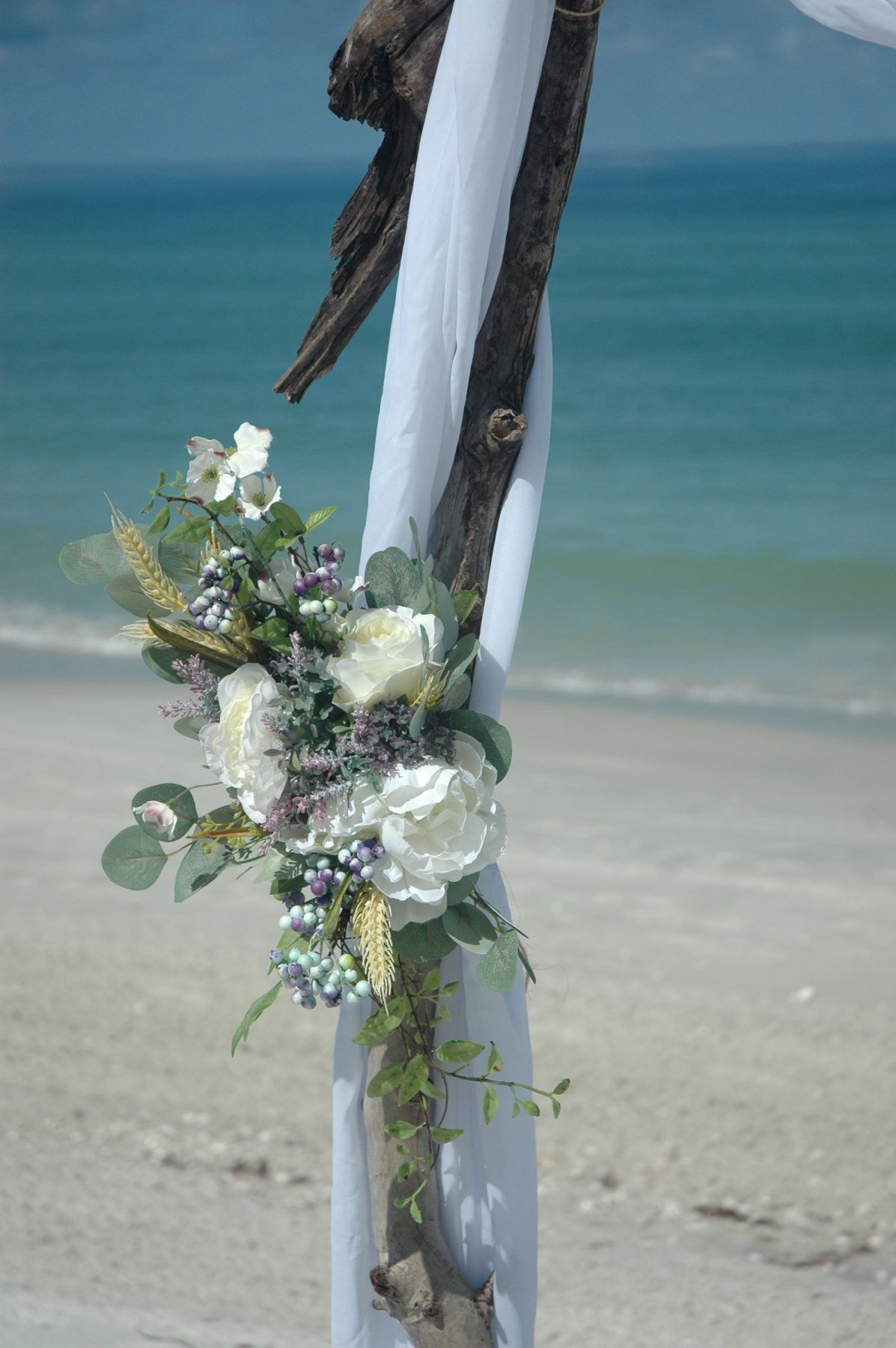 Beach wedding arch with white flowers and sheer fabric against the ocean backdrop.