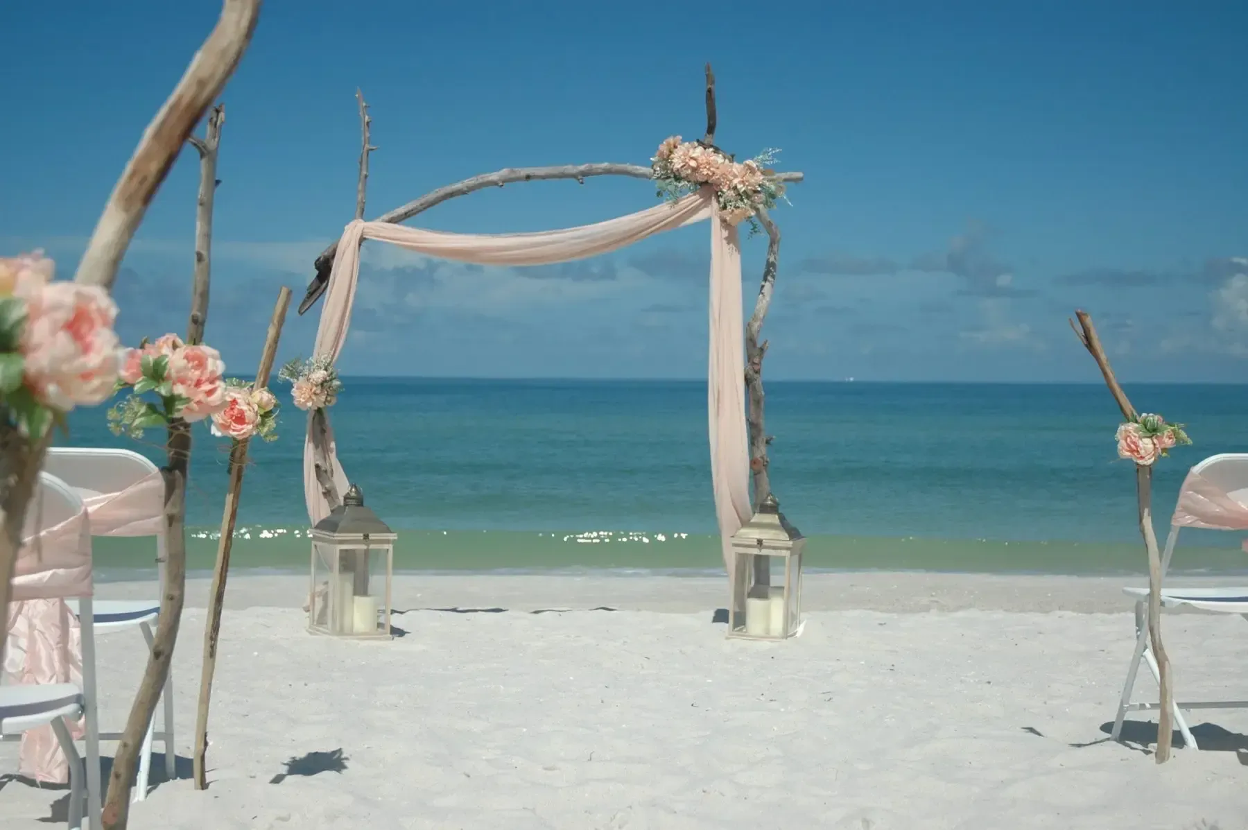 Beach wedding ceremony setup with arch, flowers, and ocean backdrop.