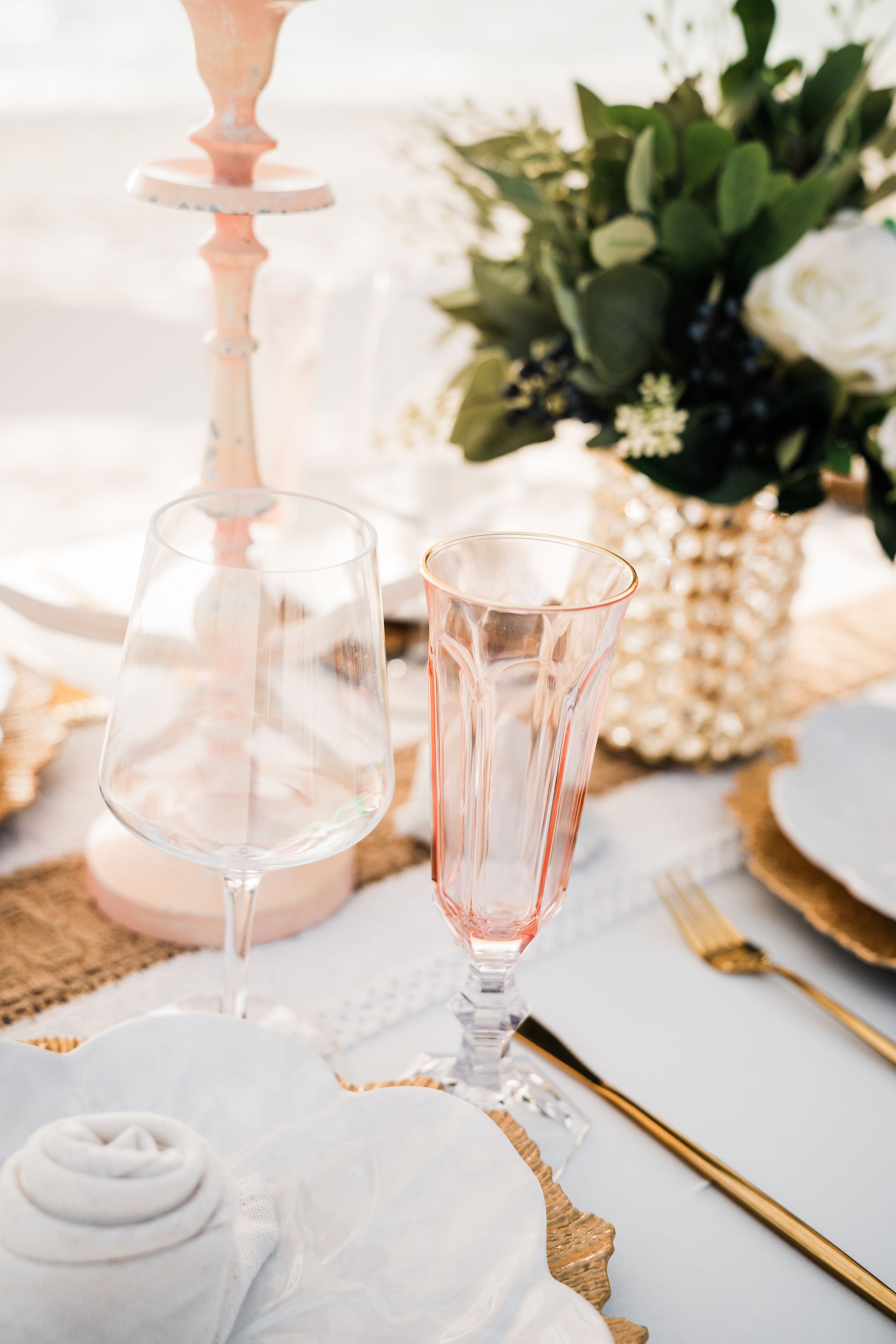 Elegant table setting with pink and gold accents; stemware, flowers, and candles.