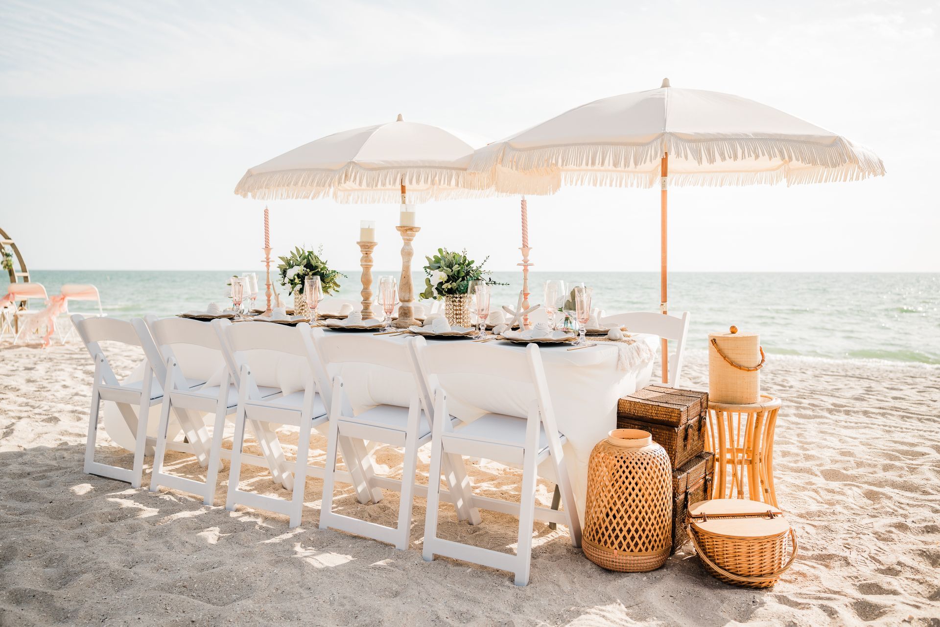 Beach table setting with white chairs, parasols, and decor.