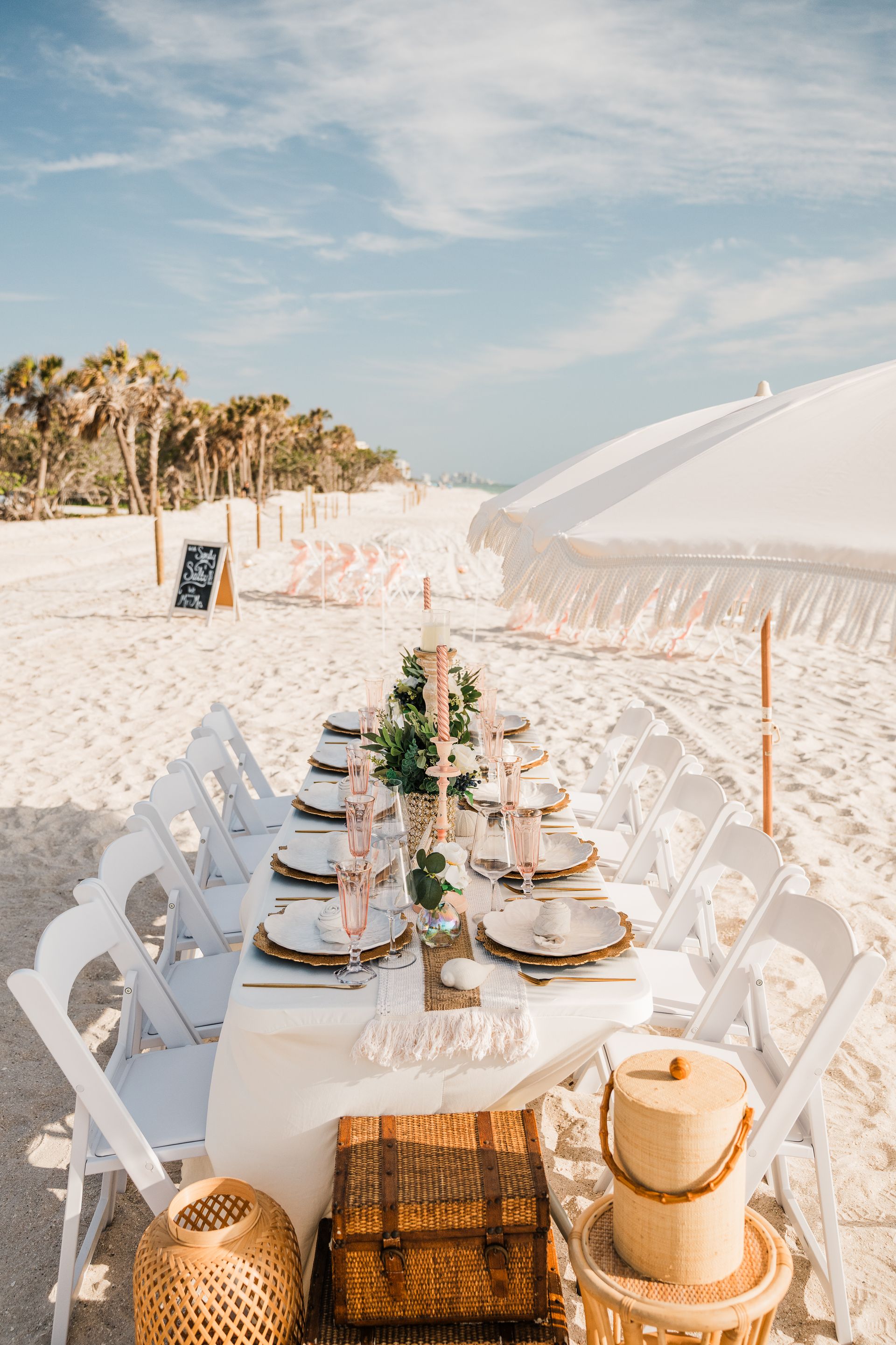 Beach dinner table set with white chairs, elegant place settings, and decorations.