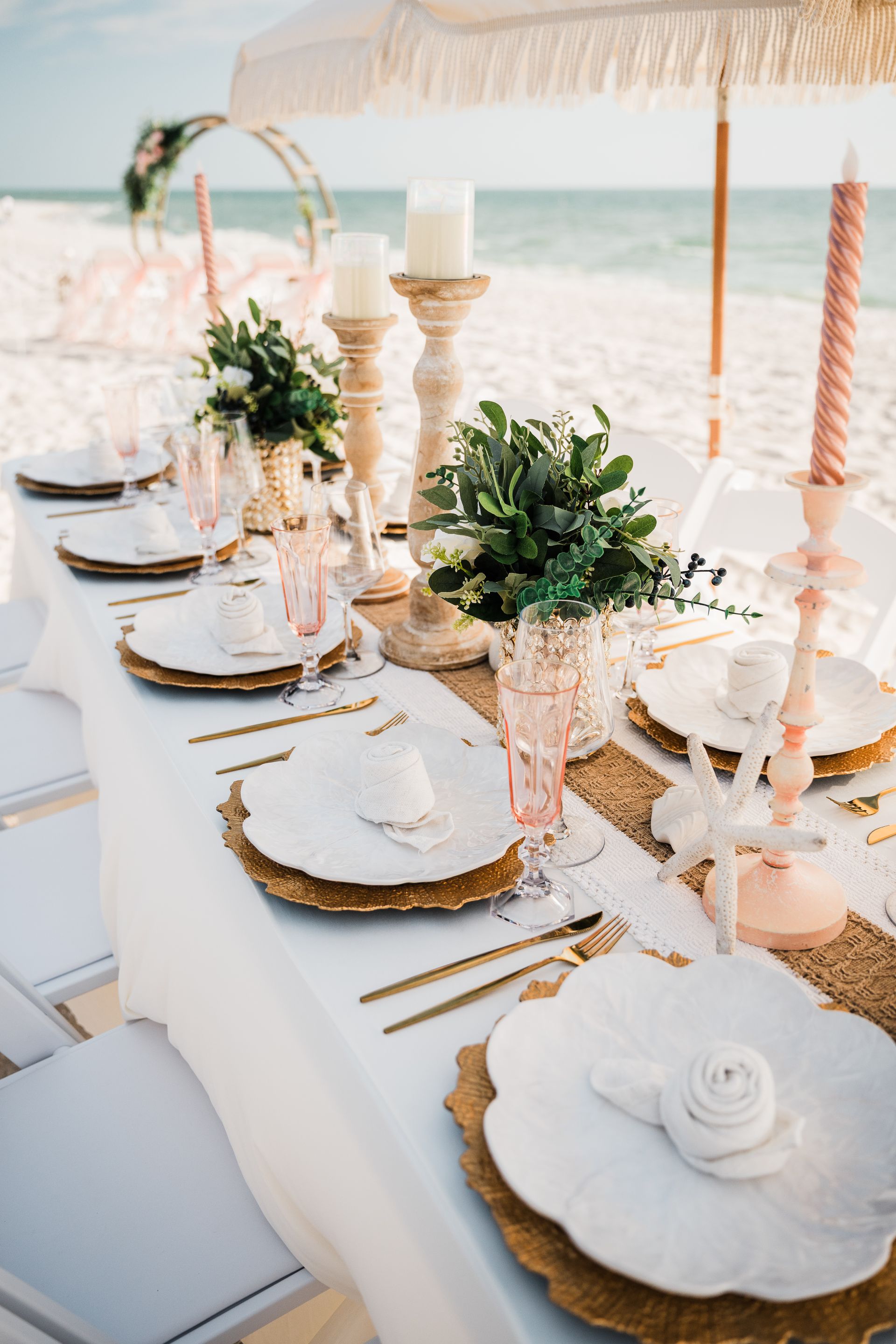 Beachside wedding reception table setting with gold and pink decor.