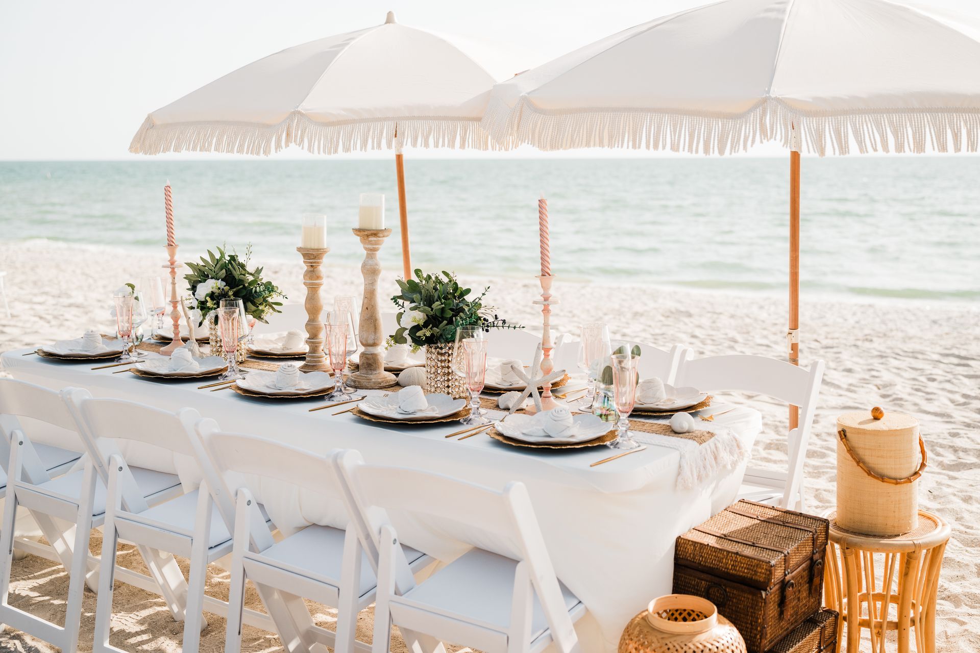 Beach table setting with white umbrellas, chairs, and decor.