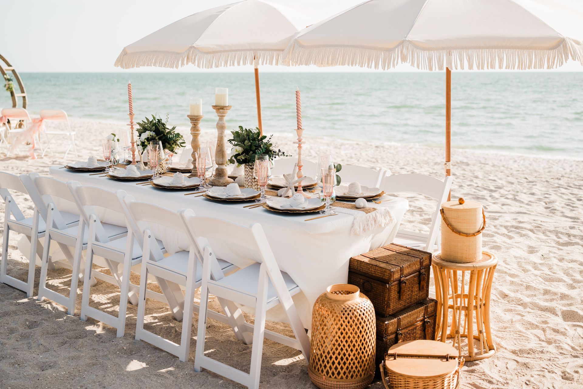 Beach table setting with white umbrellas, chairs, and decor.
